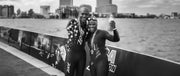 Man and woman wearing wetsuits and medals standing on a bridge