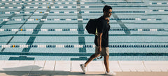 A man holding FORM Swim Goggles walking along the swimming pool