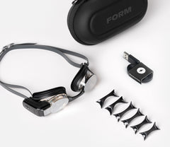 Various components of the FORM swim goggles laid out, including interchangeable nose bridges and straps.