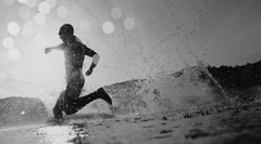 Silhouette of a triathlete running out of the water in an open water transition phase, with spray and water droplets highlighted by backlighting, emphasizing the dynamic and intense nature of the sport.