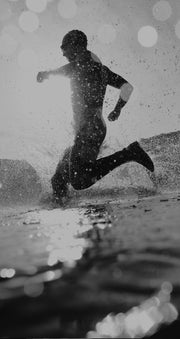 Silhouette of a triathlete running out of the water in an open water transition phase, with spray and water droplets highlighted by backlighting, emphasizing the dynamic and intense nature of the sport.