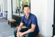 FORM CEO Dan Eisenhardt smiling sitting on a bench outside, against a concrete wall, wearing a blue shirt