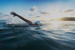 A woman in the middle of a swimming stroke taking a breath, wearing Form swim cap and Form goggles, in an open body of water 