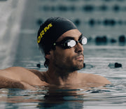 Swimmer in the water wearing FORM goggles and swim cap, looking focused and ready.