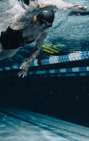 Dynamic underwater action shot of a swimmer using smart goggles, illustrating powerful swimming technique.