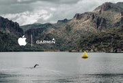 Scenic view of a swimmer in open water mode using a GPS-enabled swim tracking system, with a mountainous backdrop and a yellow buoy in the water. Logos of Garmin and Apple are displayed, indicating compatibility with these devices.